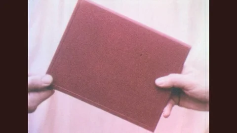 1950s: Hands hold red folder. Garden at university. Young man studies at desk Stock Footage