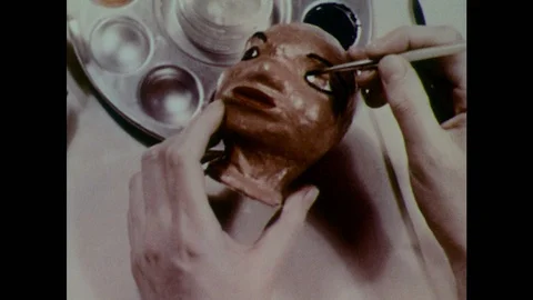 1950s: Hands paint puppet head. Hands place hair on puppet head. Stock Footage 123547300