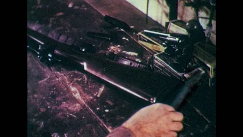1950s: Hands put tools on table, pick up gun. Man looks at gun in workshop, Stock Footage