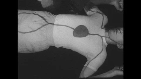 1950s: High angle view, man on ground, hands point to arteries drawn on man's Stock Footage 74931632