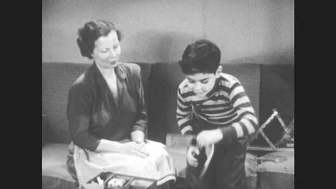 1950s: House, mother and boy sit on couch, boy picks up book, reads. Busy Stock Footage