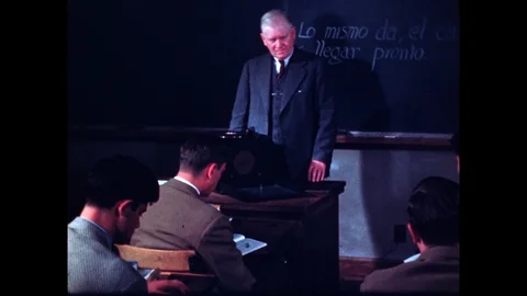 1950s: Instructor adjusts knobs on portable phonograph at desk and speaks to 스톡 동영상 110808266