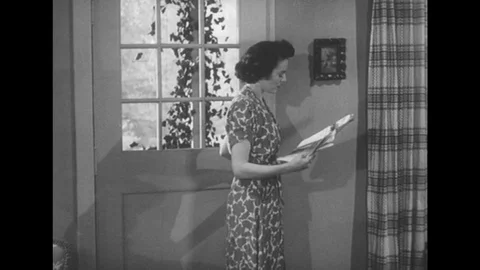 1950s: Lady shuts door and reads newspaper.Lady walks in house with newspaper. Stock Footage
