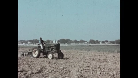 1950s: Man and boy guide ox pulling plow across field of soil. Man rides tractor Stock Footage 303587916