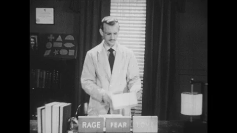 1950s: Man behind desk with three blocks on it with words: Rage, Love, Fear. He Vídeos de archivo 92860976