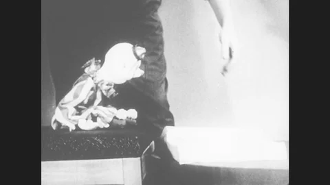1950s: Man closes book on table. Marionette clown puppet sits on chair, looks at Stock Footage 79317330