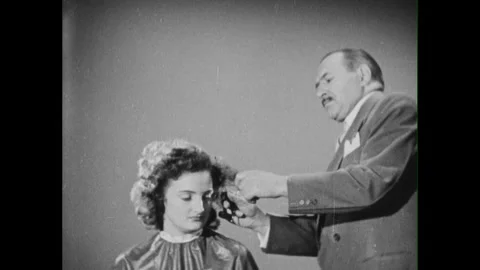 1950s: man with comb and scissors parts and combs seated woman's hair, hands Stock Footage 296503486