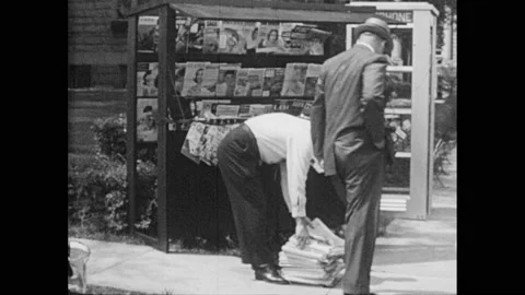 1950s: Man drops off a bundle of newspapers at a newsstand. Man buys newspaper. Stock Footage 157078812
