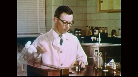 1950s: Man in lab coat, grabs vial, holds over open flame then dumps contents Stock Footage 84830081