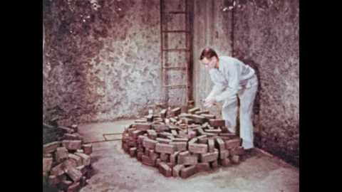 1950s: Man leans over bricks near ladder in concrete test tunnel, turns pipe 動画素材 92587671
