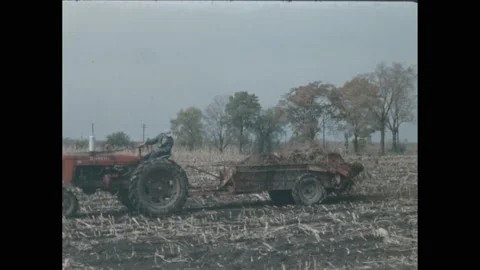1950s: Man operates tractor pulling spreader machine. Man places bags on Stock Footage 220809089