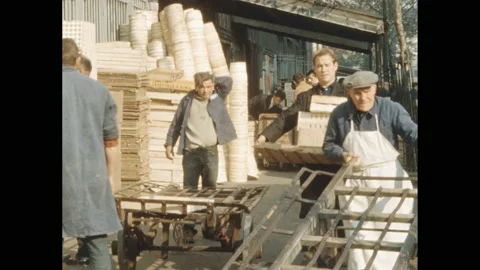 1950s: Man pulls cart with round object on it by vehicles. Men standing around Video stock 138707470