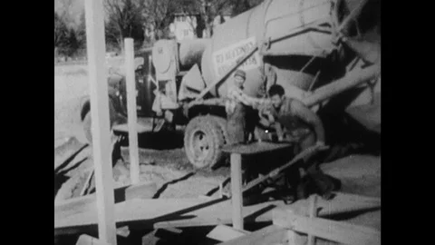 1950s: Man pushes wheelbarrow up ramp. Concrete truck unloads concrete. Crane Stock Footage 121590239