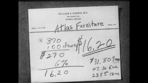 1950s: Man puts notes on finance terms on desk one at a time. Man sits at desk, Vídeo Stock 82700738