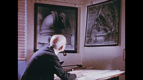 1950s: Man sits at drafting table, lokos at posters on wall, draws. Palomar Stock Footage 92589446