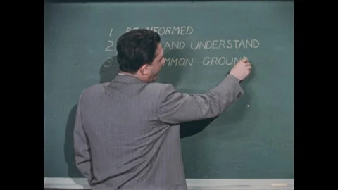 1950s: Man slaps clapper and walks away from blackboard. Man writes list on Stock Footage 273115014