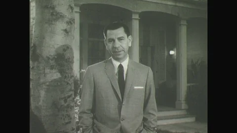 1950s: Man in suit stands in front yard of family house with hands in his Stock Footage
