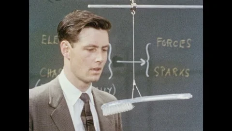 1950s: Man suspends brush on string attached to pole, rubs cloth on comb, places Video stock 84860288
