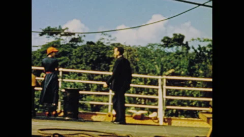 1950s: Man walks across deck of ship, stands next to woman at railing. Man and Video stock 151598568