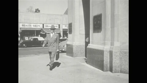 1950s: Man walks around corner of building in downtown. Man speaks. Man and Vídeos de archivo 77610628