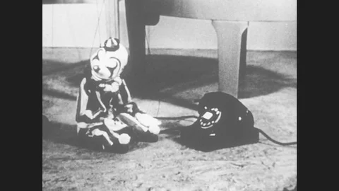 1950s: Marionette clown puppet sits in front on phone, looks around. Man removes Stock Footage 79317455