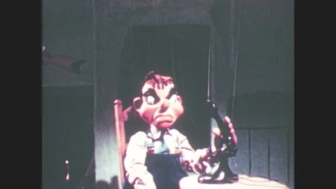 1950s: Marionette man puppet sits in chair, holds phone receiver, looks angry, Stock Footage 79474876