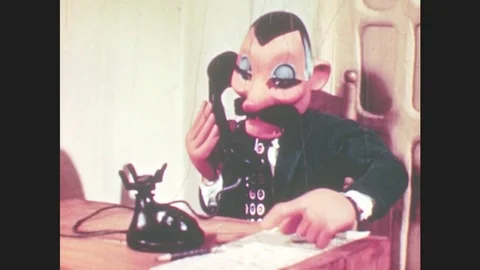 1950s: Marionette man puppet sits at desk, talks on phone. Puppet creeps across Stock Footage 79474913