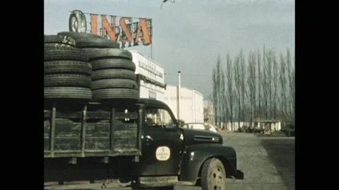 1950s: Men load tires onto back of truck near factory. Truck and men pull off Stock Footage 138673918
