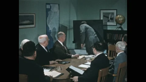 1950s: Men in suits sit around conference room table. Man stands up and shows Vídeos de archivo 238929726