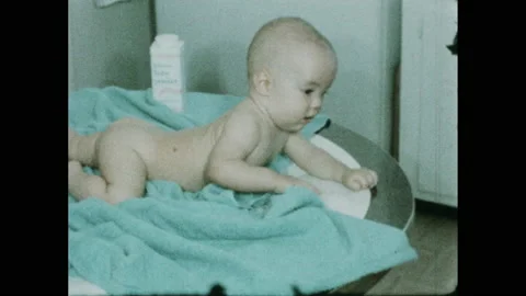 1950s: Naked baby crawls on blue towel atop table, reaches for baby powder. Stock Footage