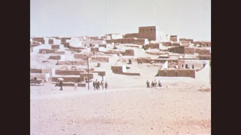 1950s: People in desert village walk towards man ringing a bell and form lines. Stock Footage
