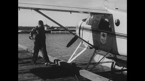 1950s: Pilot steps into a float plane parked on water and starts it up. Stock Footage 126010285