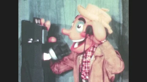 1950s: Puppet talks on payphone. Angel puppet frowns. Puppet walks from phone to Stock Footage 79474903
