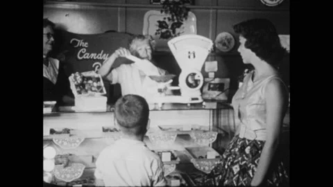 1950s: Scale at 2 pounds. Woman and boy at candy store. Woman weighs candy. Stock Footage