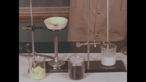 1950s: Science experiment in lab. Several glasses of elements, bowl heats over Stock Footage 272976880