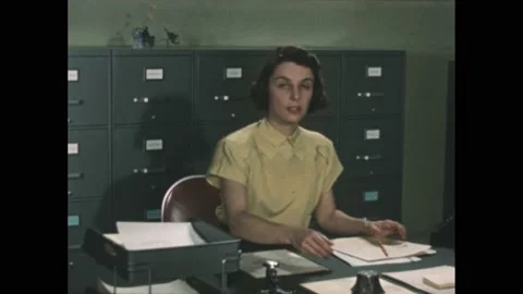 1950s: Secretary sits at a desk and ...