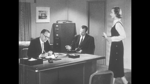 1950s: Secretary stands at mans desk ...