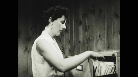 1950s: secretary taking folder out from filing cabinet to give to boss, three Stock Footage 155124784