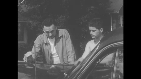 1950s: Shirtless Teen Buffs Car With Cloth. Teen And Man Talk Seriously Standing Stock Footage