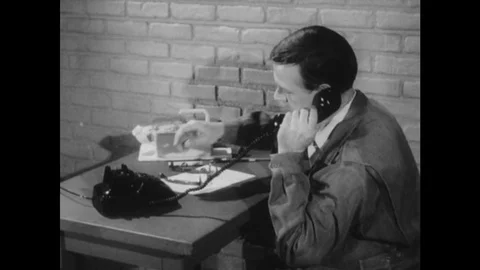 1950s: side profile as man picks up telephone on desk. Man dials phone number. Vidéo 75167200