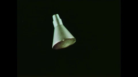 1950s- A space capsule decends, vertically, down the frame against a black Stock Footage