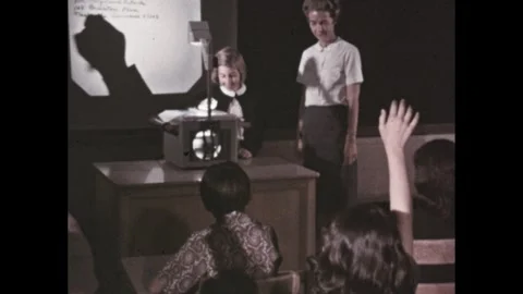 1950s: Students raise hands at desk while girl writes on overhead projector in Stock Footage 295293265