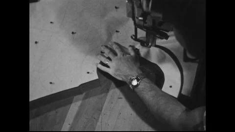1950s: A tailor cuts fabric using a rotary cutting knife. Two workers unroll Stock Footage 74534099