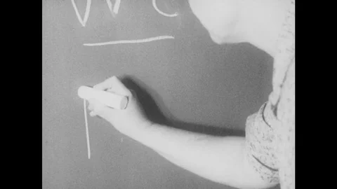 1950s: Teacher writes with large chalk. Girl with glasses. Stock Footage