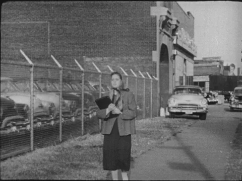 1950s: Teenage girl walks down urban street and hears siren, she asks an adult Stock Footage