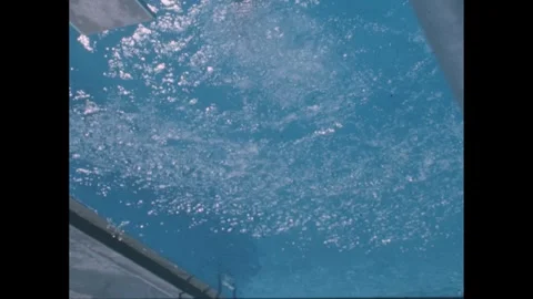 1950s: Teenagers wait at base of diving board ladder. Girl dives into pool from Stock Footage 243825835