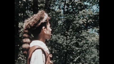 1950s: Trees and underbrush in a forest. Boy takes off his coonskin cap and Stock Footage 295296741