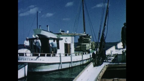 1950s: Two boats pull up next to each other. Men shovel fish onto table. Men Stock Footage 103555696