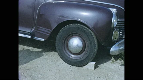 1950s: Two men approach two women fixing flat tire on car. Young man changes Stock Footage 139499151