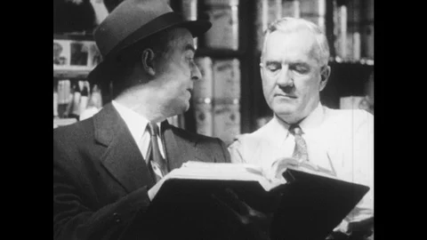 1950s: Two men read from book. Salesman demonstrates furniture cleaner to woman. Stock Footage 93325840